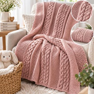 Könnte beinhalten: Eine altrosa gestrickte Wohndecke mit einem strukturierten Muster aus vertikalen Zopfstrickspalten, die sich mit Abschnitten im Perlmuster abwechseln. Die Decke liegt über einem Sessel und zeigt ihre dicke Garnstruktur und den sanften Rosaton.