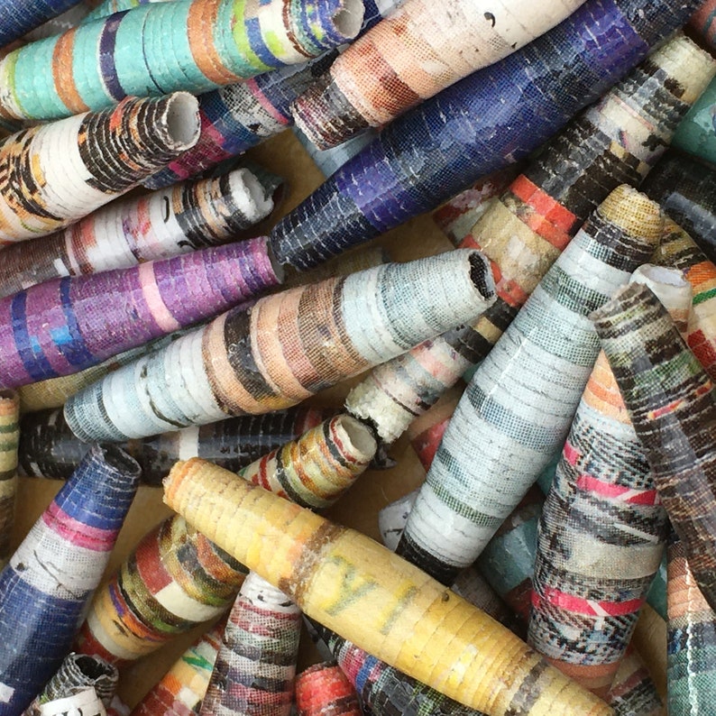 May include: A collection of colorful, handmade paper beads. The beads are made from rolled up pieces of paper and have a variety of patterns and colors, including blue, green, red, yellow, and white.
