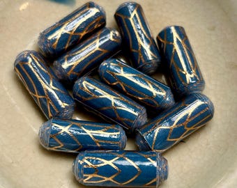 May include: A collection of cylindrical beads in a deep blue hue, adorned with a gold geometric pattern. The beads are arranged in a ceramic bowl, showcasing their intricate design and color contrast. These beads are ideal for jewelry making.