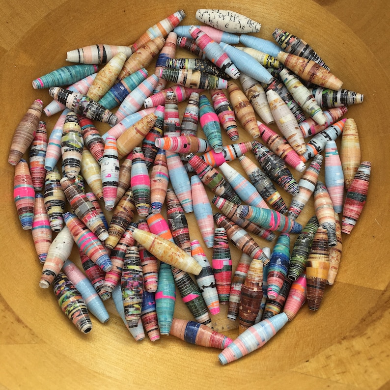 May include: A bowl filled with colorful paper beads. The beads are made from rolled up strips of paper and are decorated with various patterns and colors.