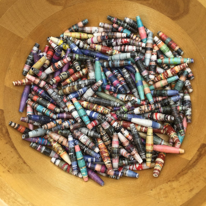 May include: A bowl filled with colorful paper beads. The beads are made from rolled up pieces of paper and are in a variety of colors and patterns.