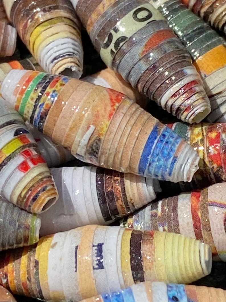 May include: Close-up of colorful, rolled paper beads. The beads are made from strips of paper that have been rolled and glued together. The beads are a variety of colors, including red, yellow, blue, green, and brown. The beads are glossy and have a slightly textured surface.