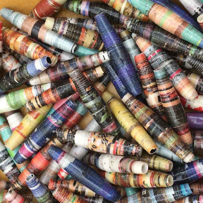 May include: A collection of colorful, handmade paper beads. The beads are made from rolled up pieces of paper, creating a unique and textured look. The beads are in a variety of colors, including blue, green, red, yellow, and brown.