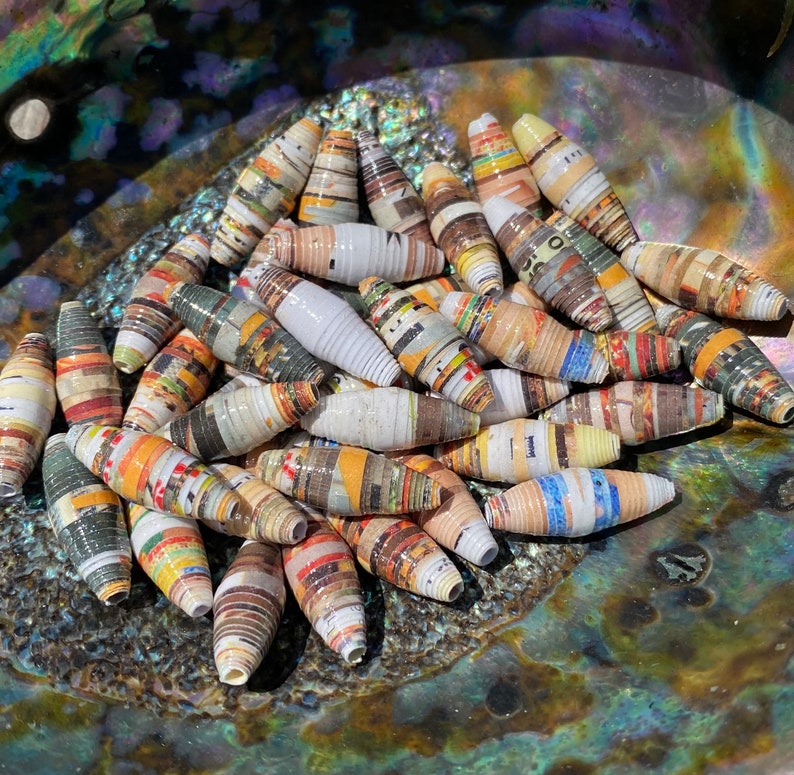 May include: A collection of colorful, handmade paper beads. The beads are made from rolled up strips of paper and have a variety of patterns and colors. They are perfect for making jewelry or other crafts.