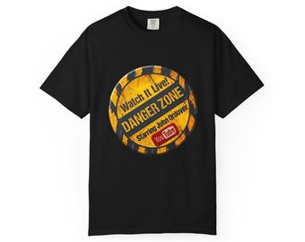 May include: A black short-sleeved t-shirt featuring a circular yellow and black hazard-style graphic. The design includes the text Watch It Live! DANGER ZONE Starring John Ordover and a red YouTube logo in the centre of the circle.