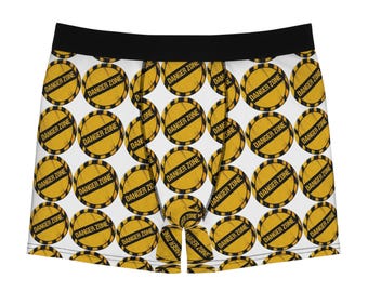 May include: Boxer briefs with a white background and a repeating pattern of circular yellow and black warning signs. Each sign features a black border with diagonal stripes and the text DANGER ZONE printed in bold black capital letters.