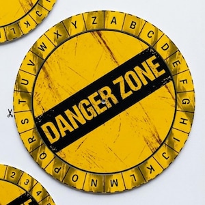 Puede incluir: Un letrero circular amarillo con textura desgastada que presenta una franja diagonal negra en el centro con el texto DANGER ZONE en letras amarillas en negrita. El borde exterior contiene el alfabeto de la A a la Z en mayúsculas negras.