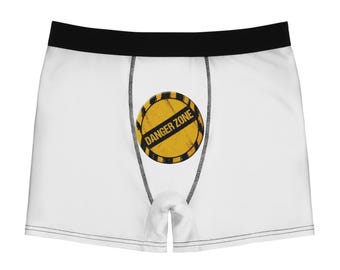 May include: White boxer briefs featuring a black waistband and a central circular graphic. The graphic is a yellow and black hazard warning sign with the text DANGER ZONE printed in bold black capital letters across the centre.