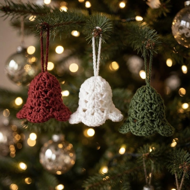 May include: Three crochet bell ornaments hanging from a tree, featuring one deep red, one white, and one dark green bell. Each bell is crafted with a textured, open-stitch pattern and includes a matching yarn loop for hanging on a branch.