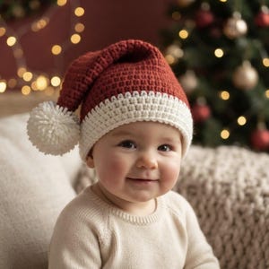 May include: A crochet Santa hat in a deep red color with a thick, textured white brim and a large, fluffy white pom-pom attached to the side. The hat is crafted with a dense, uniform stitch pattern, creating a soft and structured appearance.