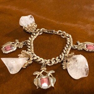 May include: A silver charm bracelet with a chain link design and multiple charms. The charms include clear quartz crystals, pink glass stones, and ornate silver designs.