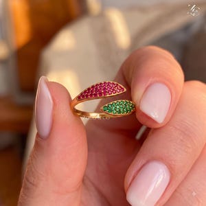 May include: A gold open-style ring featuring two leaf-shaped ends, one encrusted with small red stones and the other with small green stones. The ring is marked with the text ZODO & CO.
