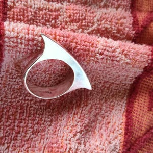 May include: A polished silver ring with a distinct, sharp, triangular fin-like protrusion extending from the top of the band. The interior of the ring band features a small, clear 925 hallmark stamp indicating sterling silver composition.