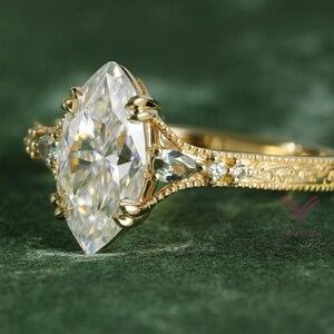 Peut inclure: Une bague en or avec une grande pierre centrale taille marquise maintenue par des griffes. L'anneau est orné de détails métalliques complexes, de petites pierres latérales en forme de poire et de minuscules pierres rondes sur le corps.