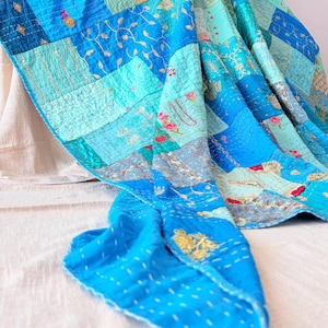 May include: A patchwork quilt featuring various shades of blue and teal fabric squares. The quilt is decorated with intricate gold embroidery, floral patterns, and small sequins, finished with visible white running stitch quilting details.