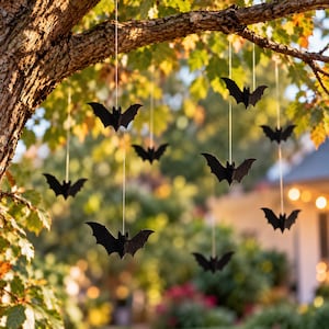 May include: A collection of black bat-shaped ornaments suspended by thin white strings from the branches of a tree. Each bat features a symmetrical silhouette with pointed ears and outstretched wings, creating a floating effect in the air.