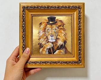 May include: An oil painting of a lion wearing a black top hat, rendered in shades of orange, brown, and gold. The lion is depicted with a paw resting on a cane. The artwork is encased in an ornate, rectangular, metallic gold frame.