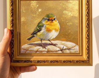 May include: A square painting of a small bird with green, yellow, and white feathers perched on a textured stone. The artwork is set in an ornate, metallic gold frame with a textured border and includes a signature in the bottom right corner.
