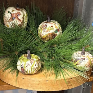May include: Four decorative ceramic pumpkins featuring detailed illustrations of game birds including ducks and pheasants, set among green pine needles. Each pumpkin has a dark brown stem and a cream-colored base with naturalistic wildlife art.
