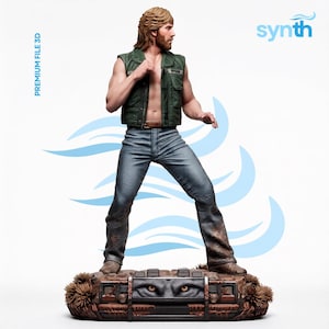 Può includere: Una statuetta dettagliata di una persona barbuta con lunghi capelli castani, che indossa un gilet verde scuro senza maniche e jeans blu. La figura poggia su una base che raffigura la parte anteriore di un veicolo con fari e il testo PREMIUM FILE 3D e synth.