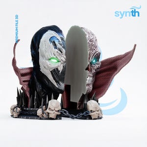 May include: A split-face bust featuring a black and white masked character on the left with glowing green eyes and a skeletal, textured face on the right with glowing blue eyes. The base is adorned with multiple skulls and a chain. Text reads PREMIUM FILE 3D.
