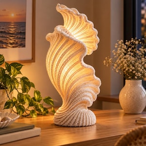 Puede incluir: Una lámpara de mesa con forma de concha marina grande y en espiral, con una superficie texturizada de color blanco roto. La lámpara emite un brillo cálido y suave desde su estructura curva y acanalada, iluminando sus relieves.