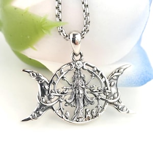May include: A silver-toned pendant necklace featuring a circular design with a central figure surrounded by tree branches, flanked by two crescent moon shapes on either side. The pendant hangs from a thick, rounded silver-toned chain link.