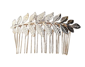 May include: A gold-toned hair comb featuring a decorative top section shaped like a branch with multiple detailed leaves. The comb has a series of thin, vertical metal prongs extending downward from the central leaf-adorned horizontal bar.