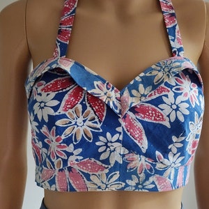 May include: A blue halter top with a floral print in shades of pink, white, and brown. The top is cropped and has a sweetheart neckline.