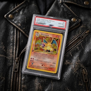 以下が含まれることがあります： 透明なプラスチックケースに入った、1999年フランス語版ポケモンカード「Dracaufeu」ホログラム1stエディション。オレンジ色のリザードンが描かれ、HP120、特性「Energy Burn」、ワザ「Fire Spin」が記載されており、GEM MT 10の評価を受けています。