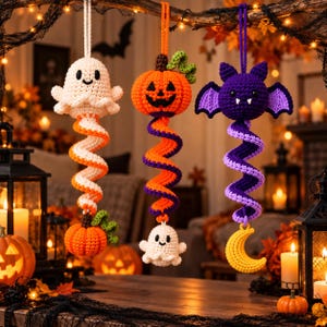Op de afbeelding: Drie hangende gehaakte ornamenten met Halloween-thema's. De eerste is een wit spookje boven een oranje pompoen. De tweede is een oranje pompoen boven een wit spookje. De derde is een paarse vleermuis boven een gele halve maan.