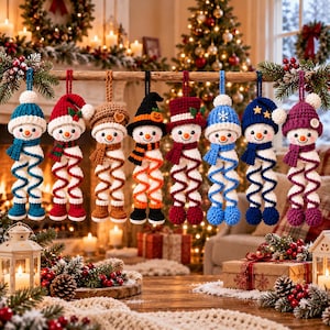 Pode incluir: Oito enfeites de boneco de neve em crochê pendurados em uma fileira. Cada boneco de neve apresenta um conjunto único de gorro e cachecol em várias cores, incluindo azul, vermelho, marrom, preto e roxo, com corpos em espiral e pés redondos.