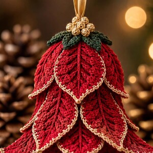May include: A crocheted Christmas ornament shaped like a bell, featuring layered red leaves with gold-trimmed edges. The top is decorated with dark green crocheted leaves and a cluster of small gold beads, suspended by a gold ribbon loop.