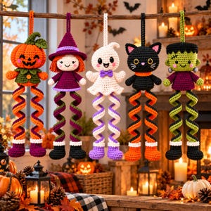 May include: Five hanging crochet ornaments featuring a pumpkin, a witch, a ghost, a black cat, and a Frankenstein monster. Each figure has long, spiraling legs and is suspended by a loop, showcasing detailed yarn work and vibrant colors.
