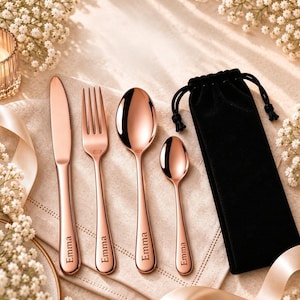 Könnte beinhalten: Ein vierteiliges Besteckset aus roségoldfarbenem Edelstahl, bestehend aus Messer, Gabel, Esslöffel und Teelöffel, jeweils mit dem eingravierten Namen Emma. Das Set wird mit einem schwarzen Samtbeutel mit Kordelzug geliefert.