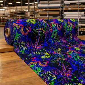 May include: A roll of fabric featuring a dark navy blue background with a vibrant, neon-colored pattern of butterflies, snakes, and abstract floral shapes in shades of bright green, electric blue, hot pink, and vivid orange throughout the print.