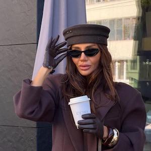 May include: A dark brown wool beret with two small silver studs, dark brown leather gloves, a dark brown blazer, and black oval sunglasses. A white paper coffee cup features the Cyrillic text "ІСТЕТИКА" in black lettering.