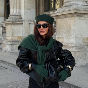 Puede incluir: Una boina verde oscuro, un suéter verde oscuro sobre los hombros, guantes verde oscuro, una chaqueta de cuero negra con mangas abullonadas, pantalones negros, gafas de sol negras y un bolso de cuero negro con detalles en tono dorado.