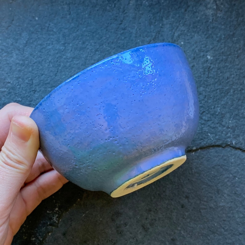 May include: A small, blue ceramic bowl with a speckled glaze. The bowl has a slightly rounded bottom and a smooth, glossy finish.