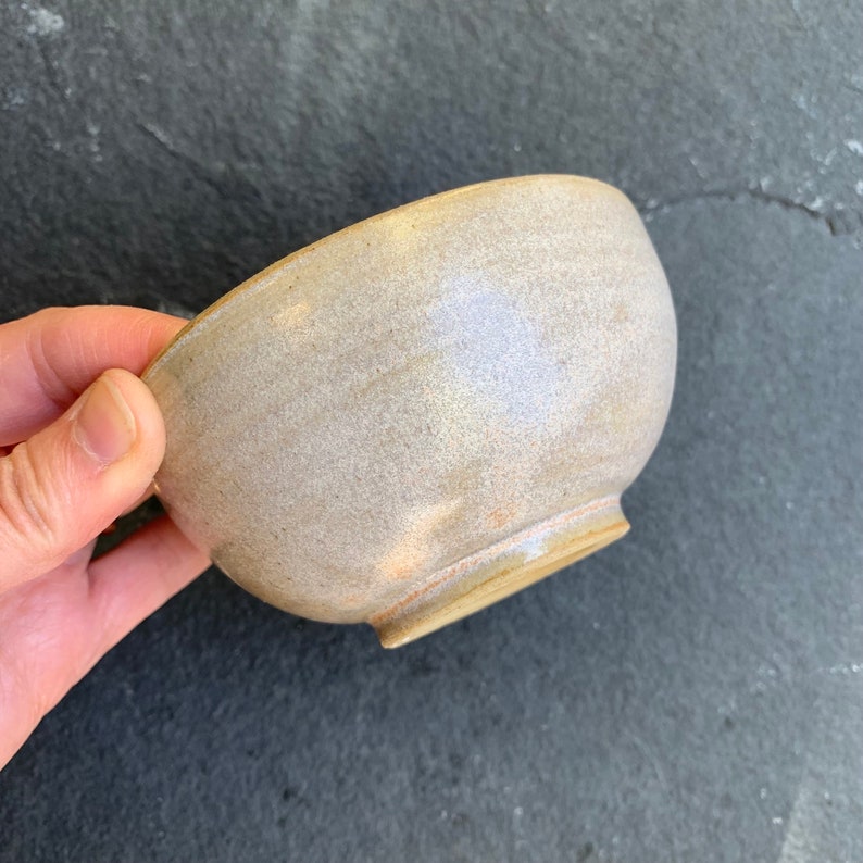 May include: A small, off-white ceramic bowl with a slightly textured surface. The bowl has a rounded shape and a slightly flared rim.