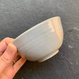 May include: A light gray ceramic bowl with a slightly uneven glaze. The bowl is slightly wider at the top than the bottom.