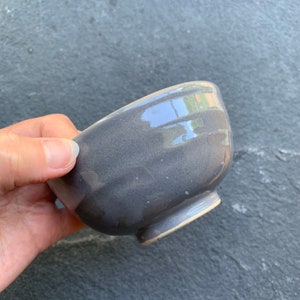 May include: A small, gray ceramic bowl with a glossy finish. The bowl has a slightly rounded shape and a wide rim.