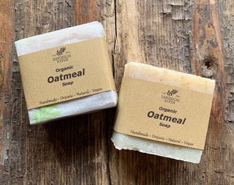 May include: Two bars of organic oatmeal soap, wrapped in paper with a brown label. The label reads "Organic Oatmeal Soap" and "Handmade - Organic - Natural - Vegan". The soap is on a rustic wooden surface.