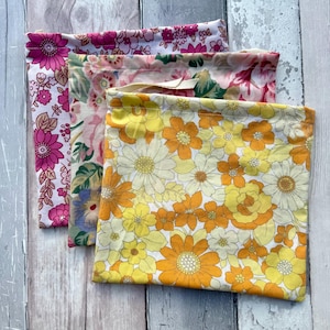 May include: Three fabric bags with floral patterns. The bags feature pink, yellow, and orange flowers. The patterns include large and small flowers, set against a white background.
