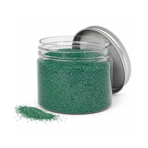 Open clear jar of emerald green colored quartz sand with its silver metal screw lid leaning behind it and a small pile of the same sand spilled in front, showing the fine grain texture, on a white background.