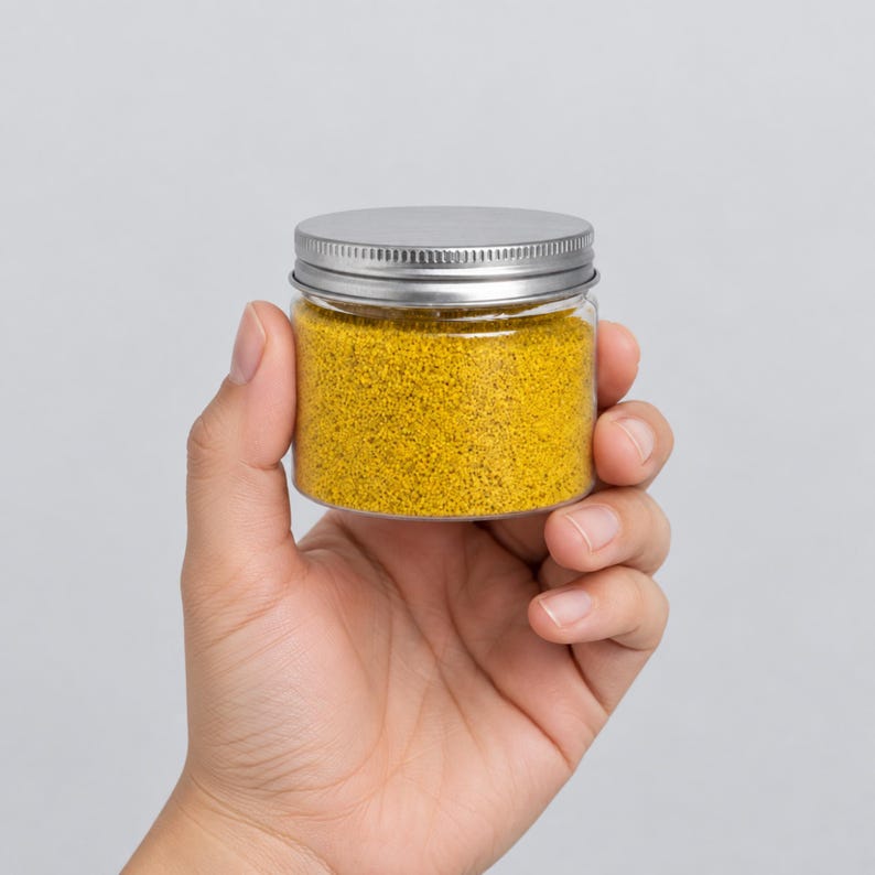 Hand holding a small closed jar of Golden Saffron yellow craft sand with a silver lid to show size