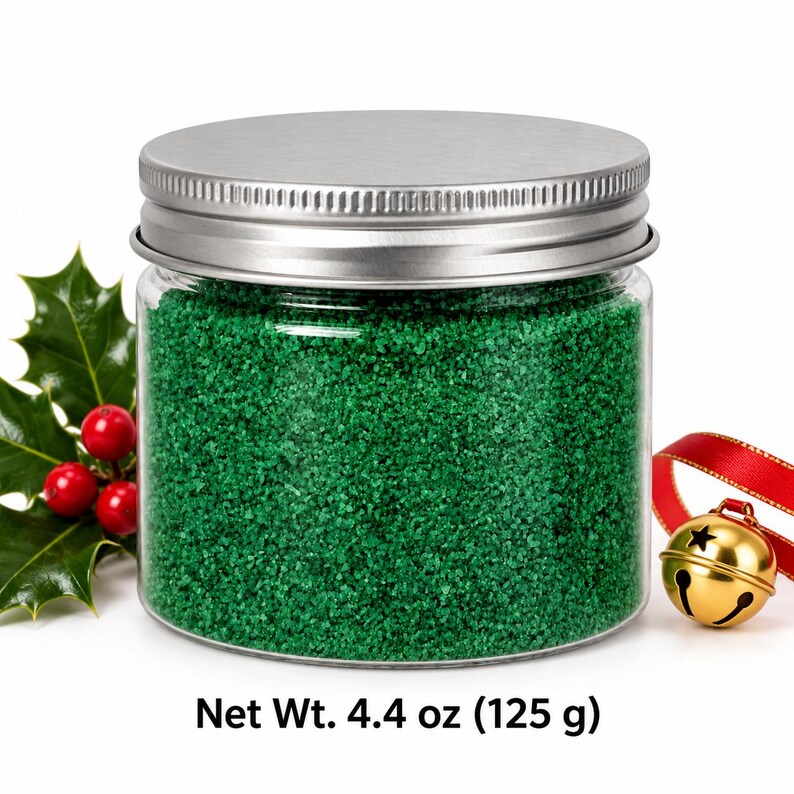 Closed clear jar of Lagoon Green colored quartz sand in a bright emerald green, with a silver metal screw lid, next to holly leaves with red berries and a gold jingle bell on a red ribbon, with text: Net Wt. 4.4 oz (125 g).