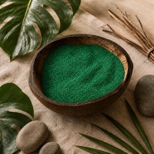 Wooden bowl filled with green craft sand, surrounded by tropical leaves and smooth stones