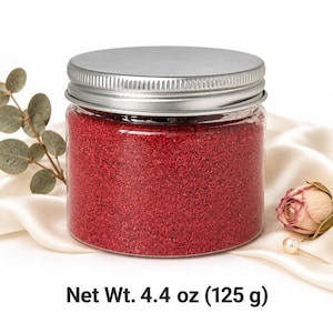 Closed clear jar of warm orange colored quartz sand with a silver metal screw lid, next to autumn oak leaves and a small orange pumpkin, with text: Net Wt. 4.4 oz (125 g).