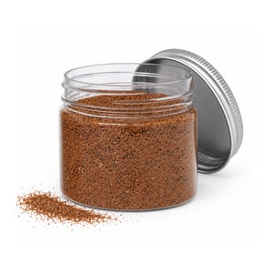 Open clear jar of warm reddish brown colored quartz sand with its silver metal screw lid leaning behind it and a small pile of the same sand spilled in front, showing the fine grain texture, on a white background.
